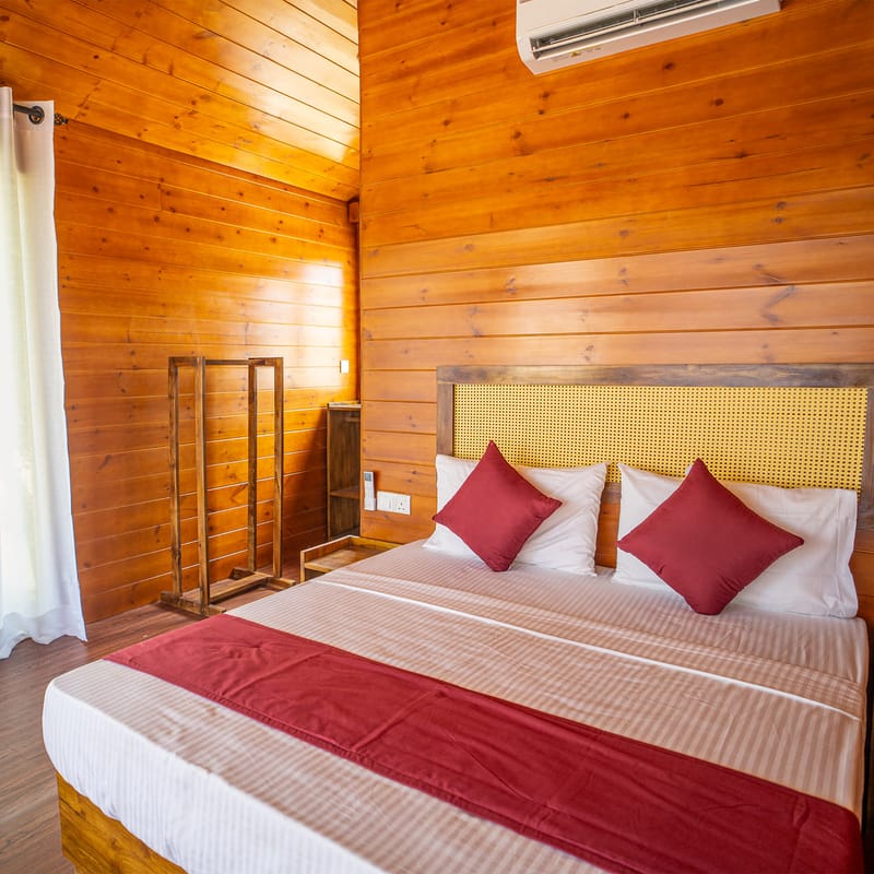 A timber-panelled villa bedroom at Arugam Bay with a cane headboard and light curtains